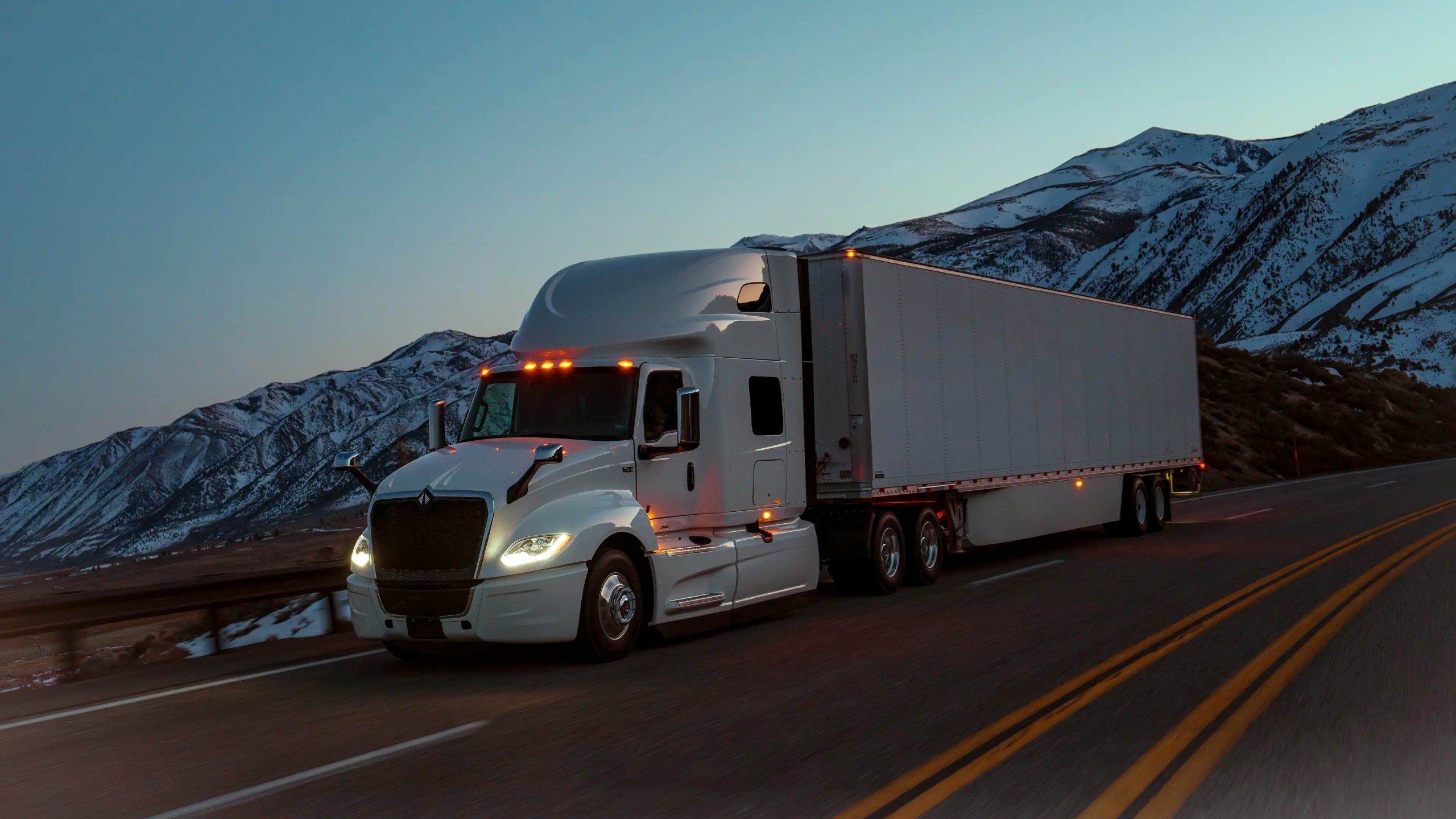 Tractocamión International LT con caja seca en una carretera de montaña con nieve al atardecer